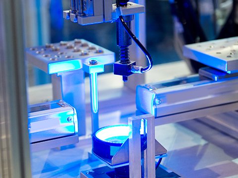 Precision automated inspection station with a component under bright blue illumination, representing the use of AI vision for quality control, alignment, and defect detection in the optoelectronics industry.
