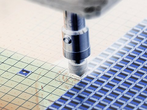Close-up of a high-precision robotic end-effector placing or manipulating a die (chip) onto a grid of wafers or micro-components, illustrating the use of AI vision for wafer inspection, micro-assembly, and quality control in the semiconductor industry.